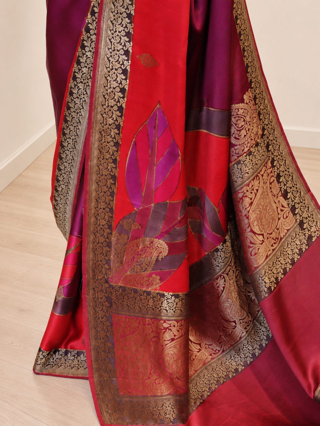 Wine magenta with contrasting red, orange and pink sections, highlighted by gold-toned zari. Katan Silk Banarasi saree border closeup